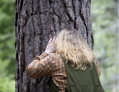 Kvinna i skogskläder kramar ett träd i en skog. Foto: @ Camilla Zilo