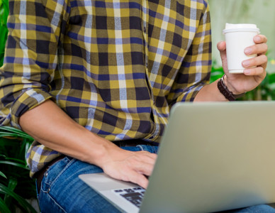 Person i rutig skjorta sitter med en laptop och håller i en kaffemugg. Foto: MostPhotos