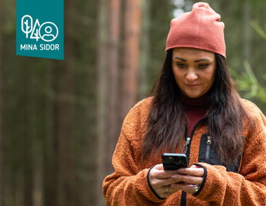 Kvinna i skog tittar på mobiltelefon.