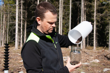 Man i skog häller jord från en vit behållare ner i en glasburk. Man i skog häller jord från en vit behållare ner i en glasburk.