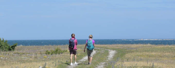 Två vandrare går på en stig mot havet på en solig dag.