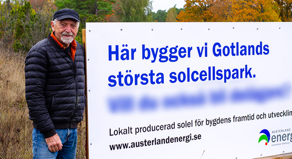 Wolgang Brunner står vid en skylt. På skylten står det "Här bygger vi Gotlands största solcellspark." samt "www.austerlandenergi.se".