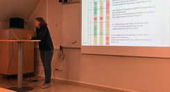 Kvinna presenterar vid en föreläsning med en PowerPoint-presentation i bakgrunden.