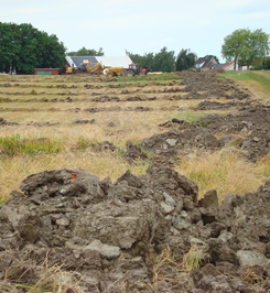Plöjt fält med lantbruksmaskiner i bakgrunden. Plöjt fält med lantbruksmaskiner i bakgrunden.