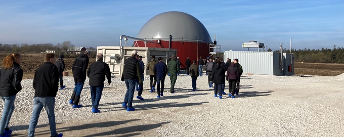 Flera personer går mot en större kupolformad byggnad i lantbruksmiljö.
