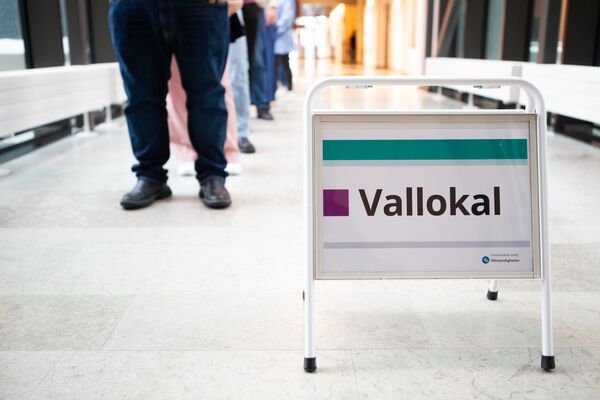 Skylt med texten Vallokal framför en kö med personer i en korridor