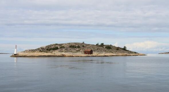 Låg klippö med fyr och röd stuga vid stilla hav under molnig himmel.