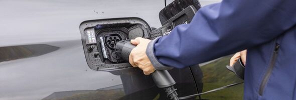 Närbild på när en hand kopplar in laddsladden till en elbil. 