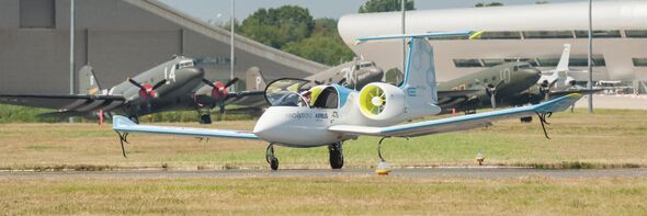 Elflyg på landningsbana med militära flygplan i bakgrunden.