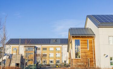 Flerbostadshus med solpaneler under klarblå himmel.