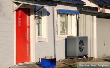 Vit tegelvilla med röd ytterdörr och en luftvärmepump vid garaget