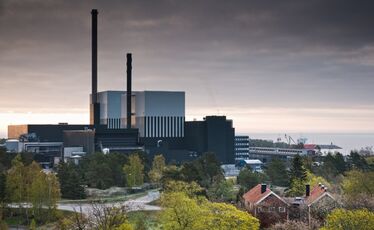 Kraftverk med två skorstenar vid kustlandskap och villor i förgrunden