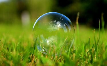 Genomskinlig tvålbubbla i gräs med reflektion av himlen